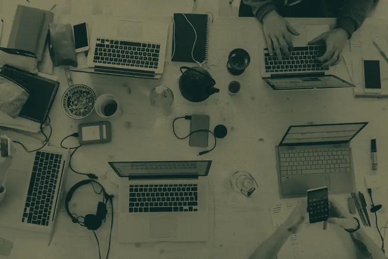A desk covered with laptops, a phone and cables, seen from above.